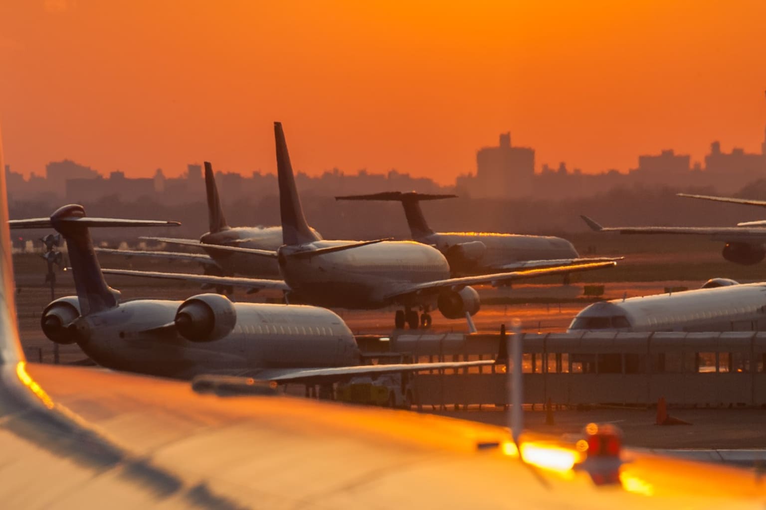 Regional jets lined up for departure at sunset with a city skyline behind them