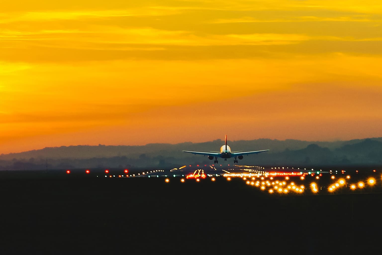 Un avión de línea en final corta al atardecer, con las luces de aproximación encendidas a lo largo de la pista
