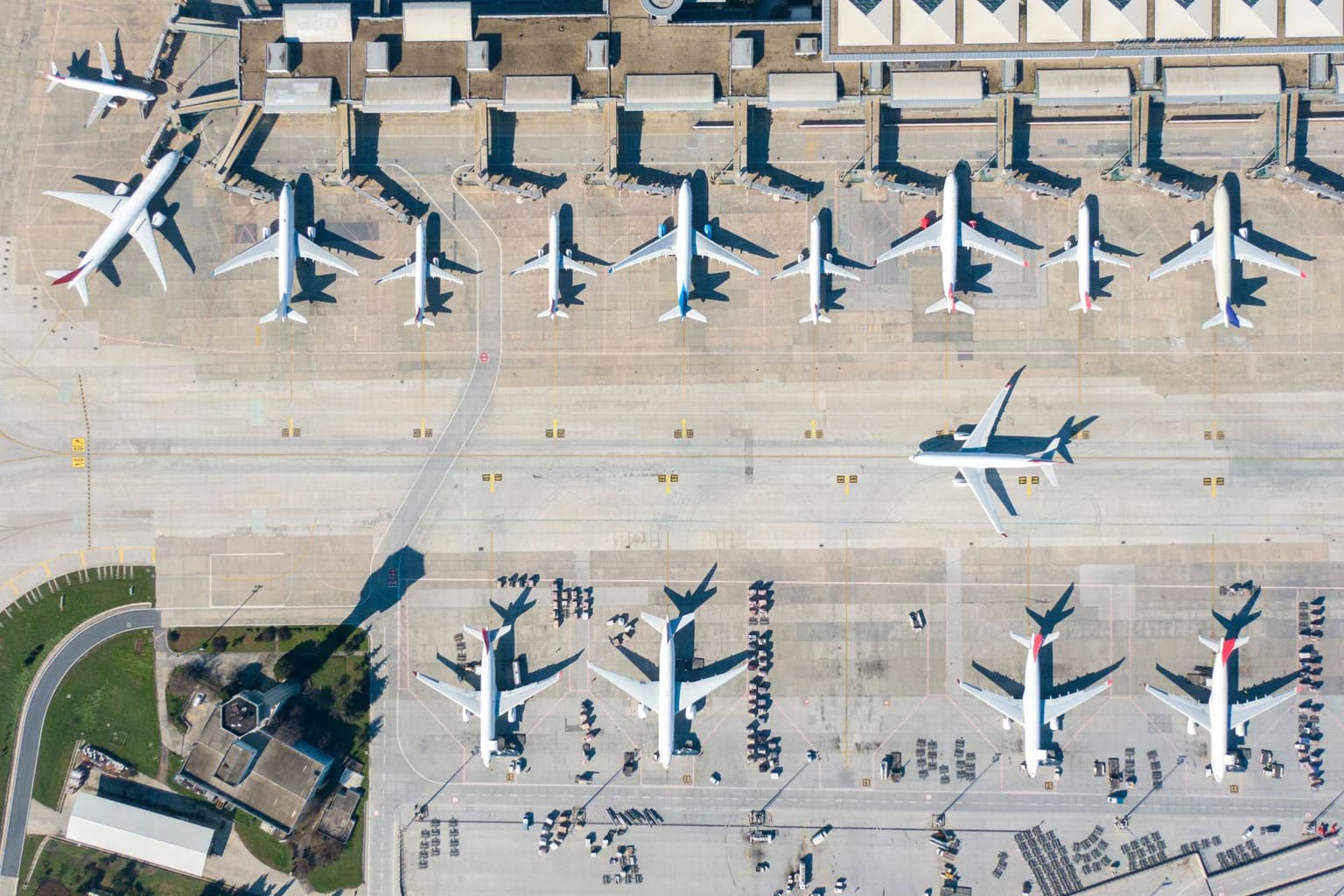 Aviones de línea estacionados en fila en las puertas de embarque, vistos desde arriba, con una aeronave en retroceso hacia la calle de rodaje para salir